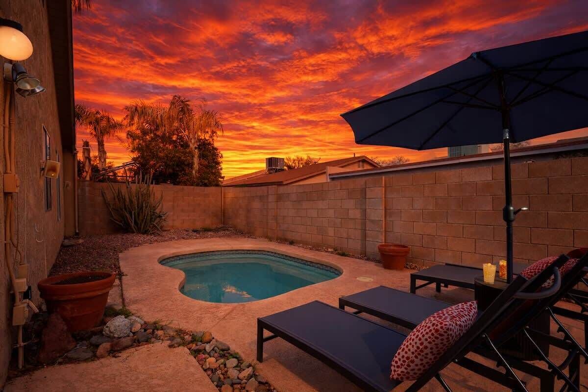 A backyard with a swimming pool, lounge chairs, and an umbrella.