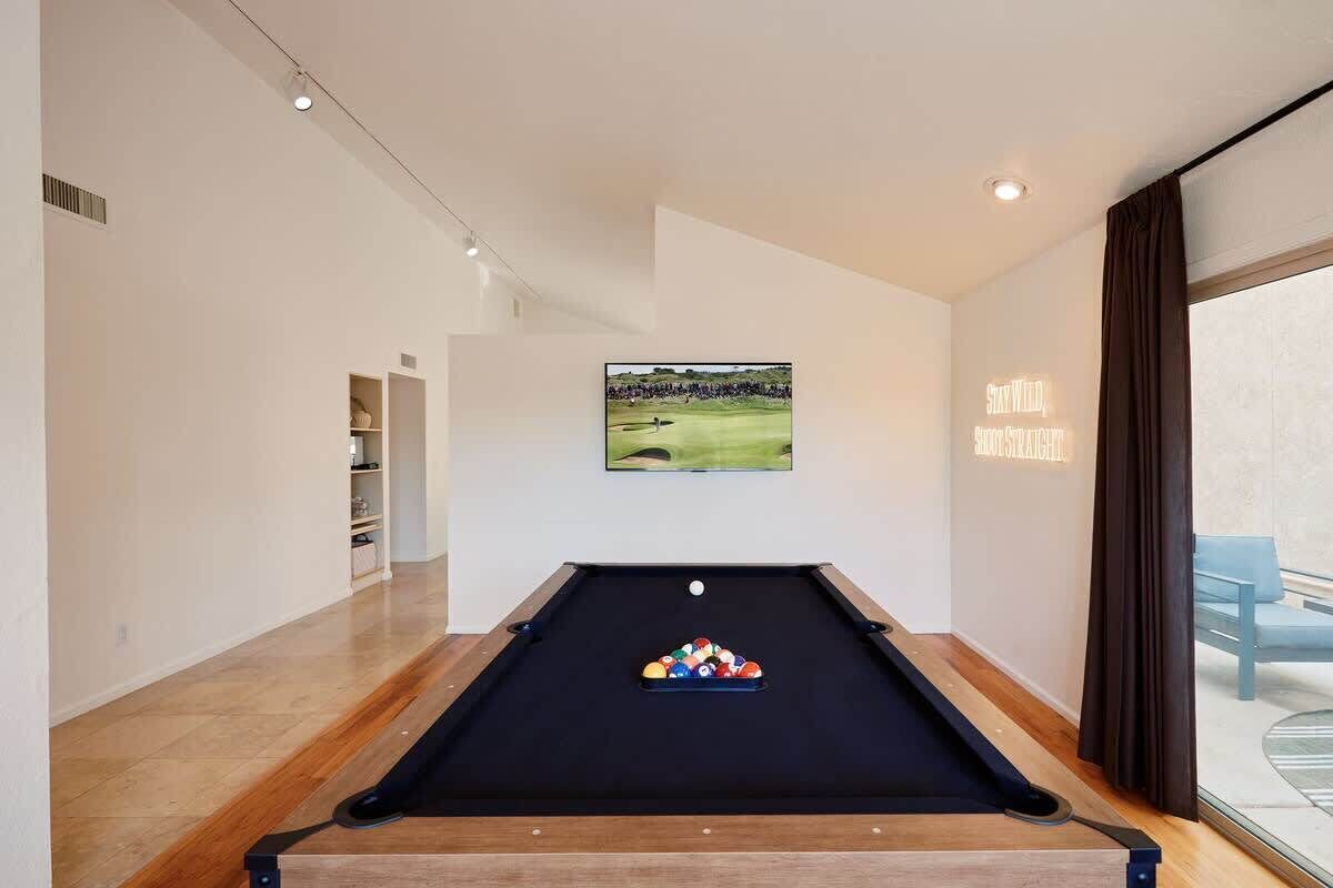 A pool table with balls, a framed picture on the wall, and a view of a golf course through a window.