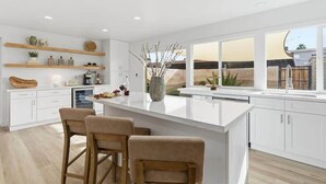 A modern kitchen with white cabinetry, a large island with bar stools, and a view of the backyard through large windows. - Hideaway - In Old Town Scottsdale-Walk to Downtown (Scottsdale)