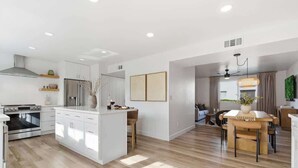 A modern kitchen with white cabinetry, a central island, and a dining area with a wooden table and chairs. - Hideaway - In Old Town Scottsdale-Walk to Downtown (Scottsdale)