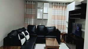 Un soggiorno con un divano nero, due tavolini in legno, una TV su un mobile e tende a righe.