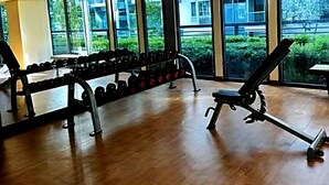 Un'ampia palestra con ampie finestre, pavimento in legno e diverse attrezzature per esercizi, tra cui manubri e panche.