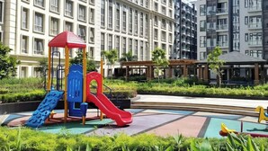 Un'area giochi con scivoli e strutture di arrampicata, circondata da verde curato e moderni palazzi condominiali sullo sfondo.