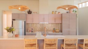 Une cuisine moderne avec des meubles de couleur claire, un îlot central doté de chaises et des luminaires suspendus.