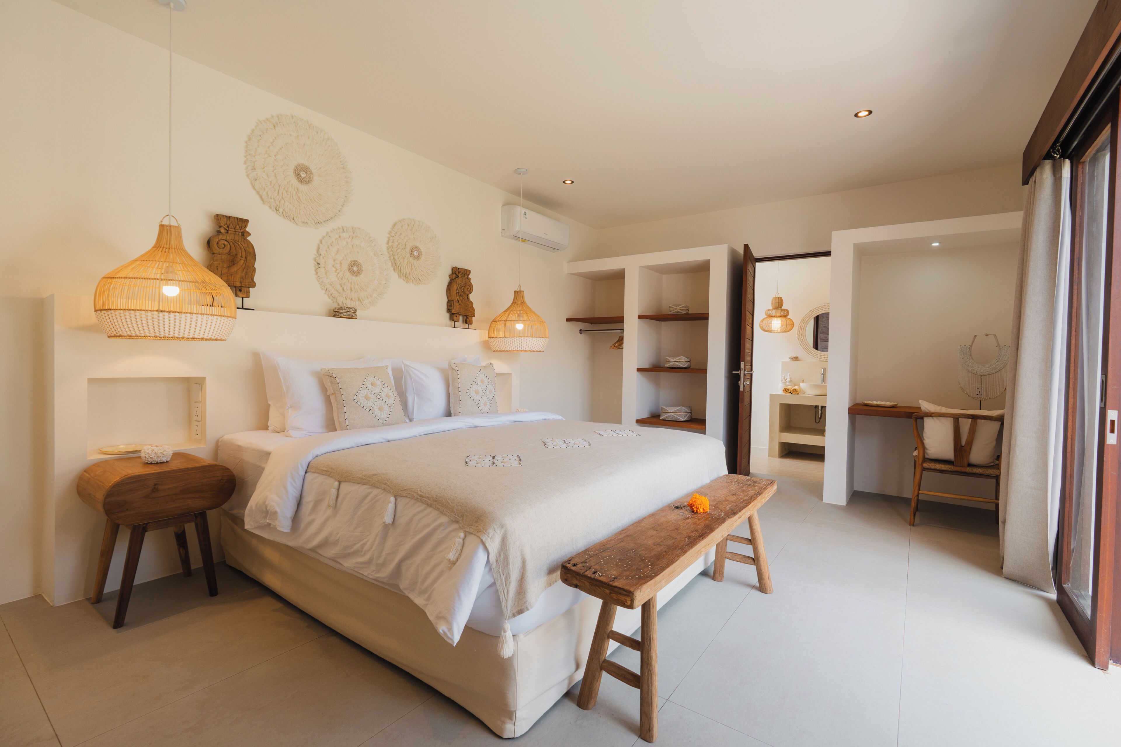 A bedroom with a large bed, bedside tables, a wooden bench, and a desk with chairs.
