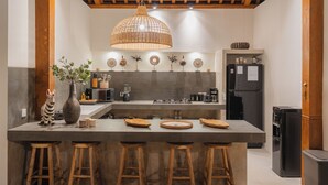 A kitchen with a central island, stools, a hanging light fixture, and a refrigerator. - Villa Oomi by Alfred in Bali (Seminyak)