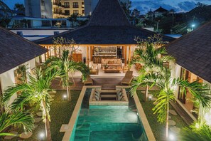 A pool area with a lounge chair and a sofa, surrounded by palm trees and a thatched-roof structure. - Villa Oomi by Alfred in Bali (Seminyak)