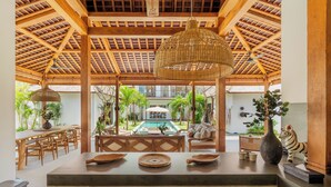 A spacious indoor area with a wooden ceiling, a central dining table, and a view of an outdoor swimming pool. - Villa Oomi by Alfred in Bali (Seminyak)
