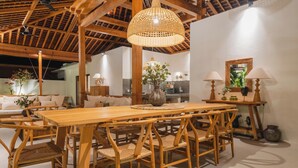 A dining area with a wooden table and chairs, a hanging light fixture, and a mirror on the wall. - Villa Oomi by Alfred in Bali (Seminyak)