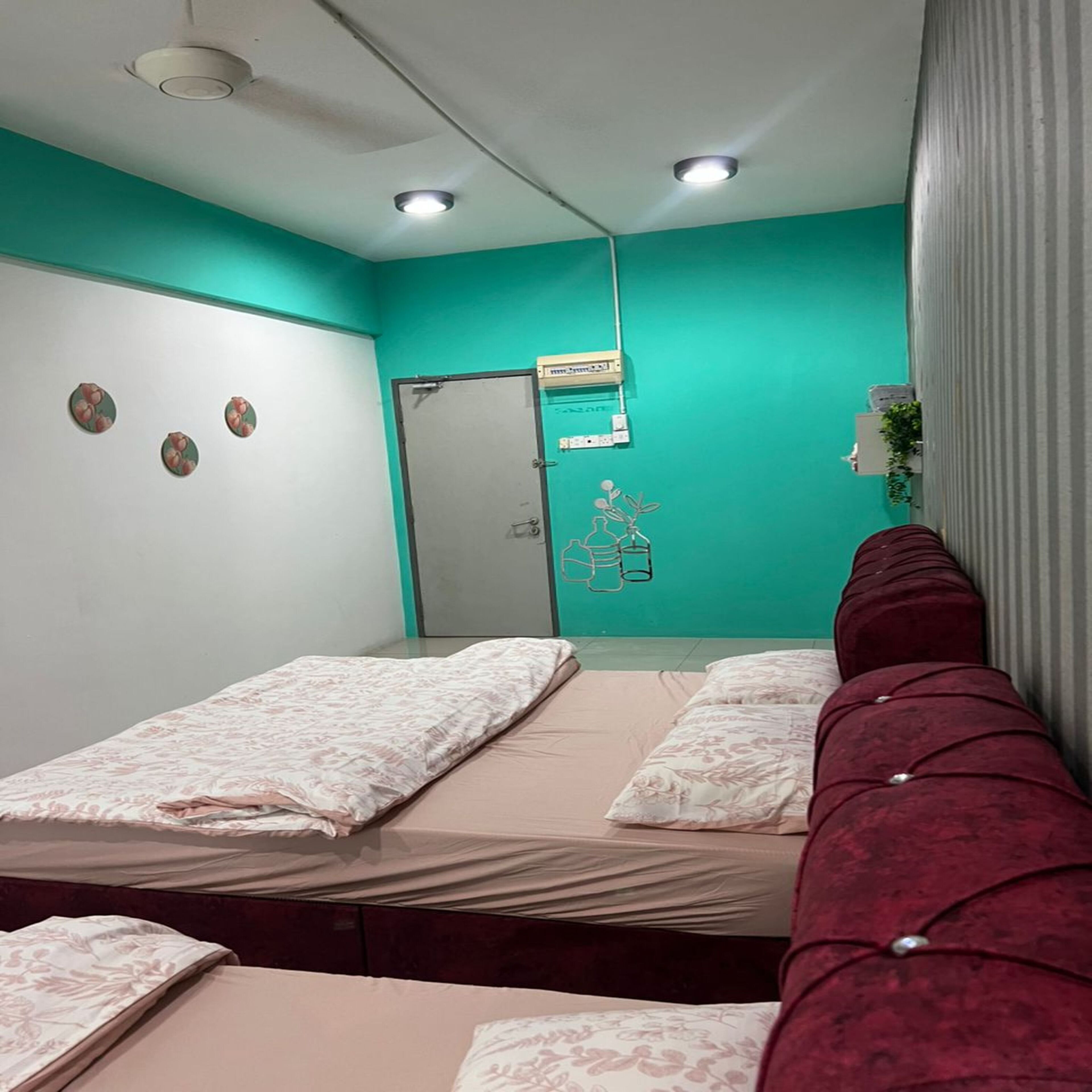 Ein Zimmer mit zwei Betten, türkisfarbenen Wänden und einer Tür, an deren Wand ein medizinisches Gerät angebracht ist.
