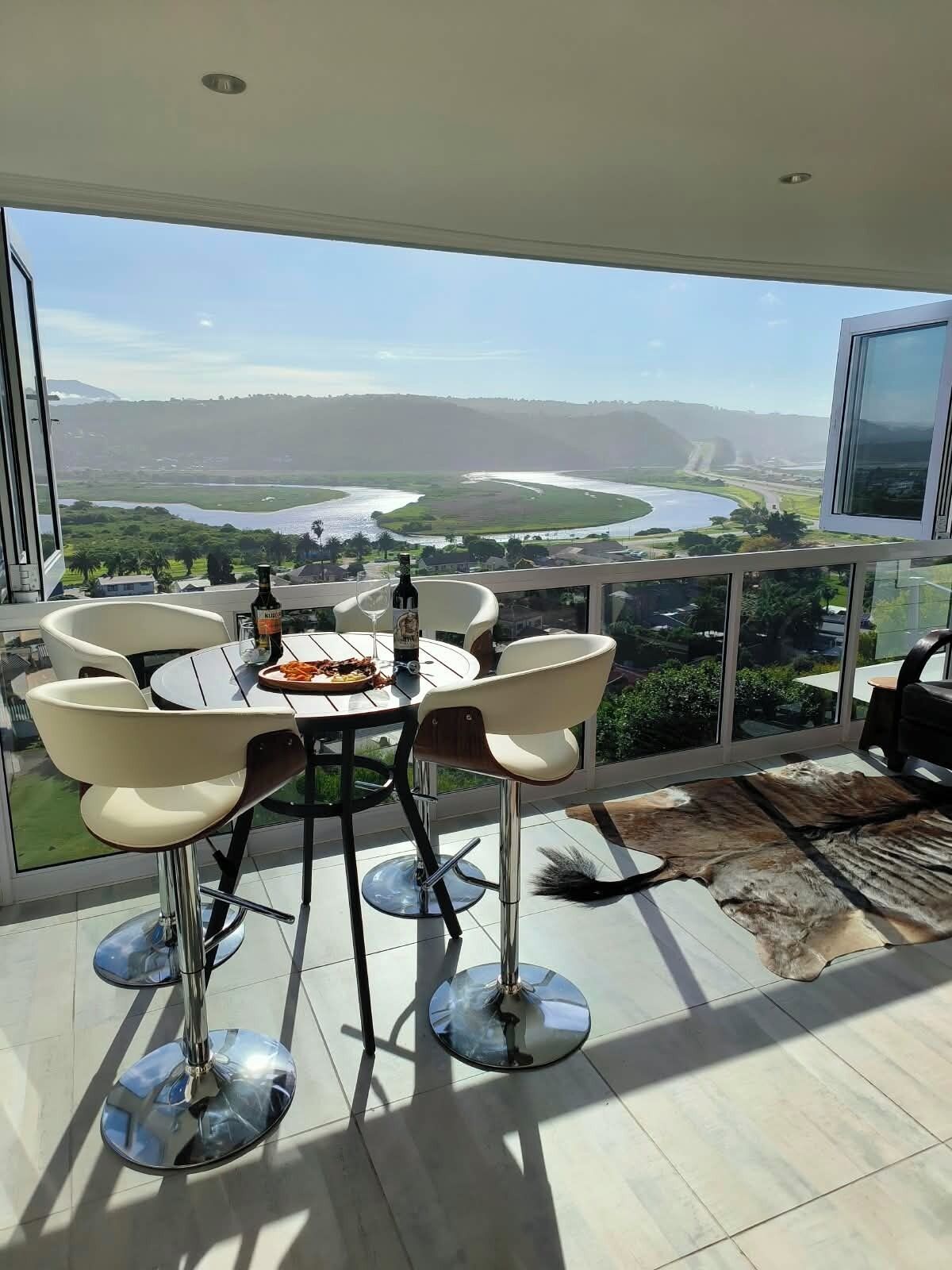 A dining area with a table and chairs, a bottle of liquor, and a view of a river and landscape.