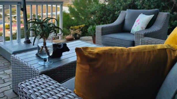 A covered outdoor seating area with wicker furniture, a potted plant, and a view of the landscape.