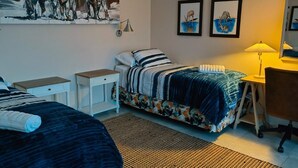 A bedroom with two beds, a desk, a chair, a lamp, and artwork on the walls.