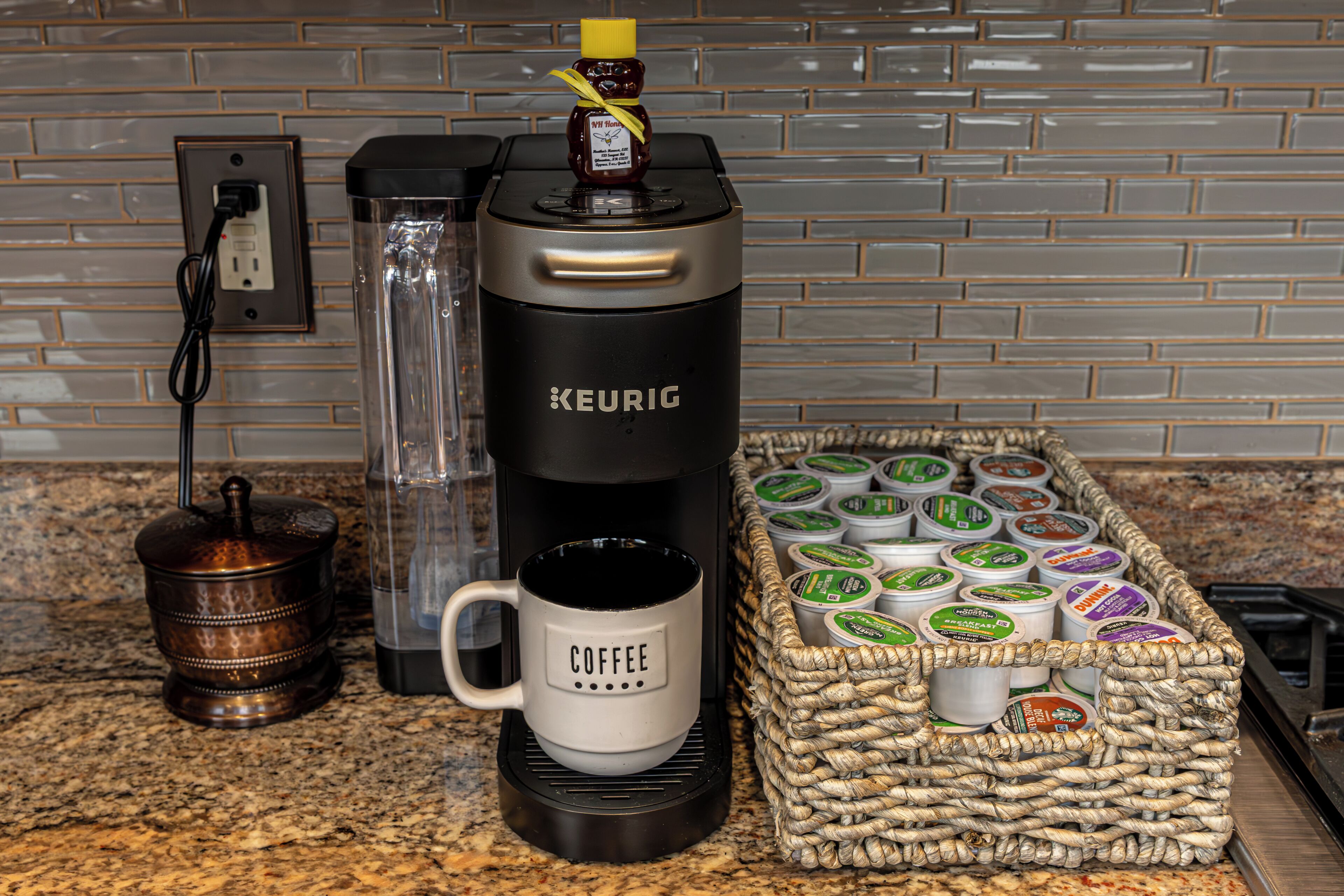 A coffee maker, a mug, and a basket of coffee pods on a kitchen counter.