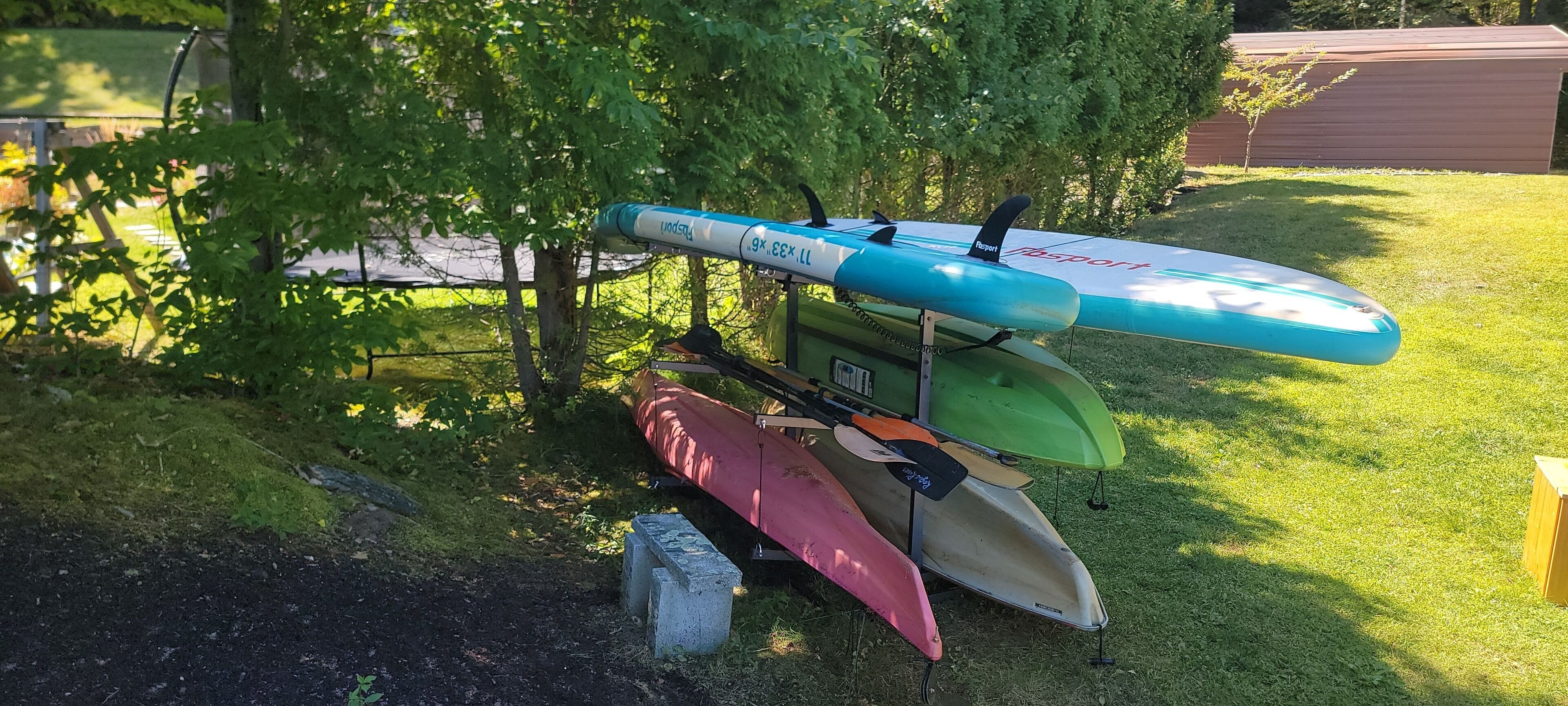Eine Reihe von Kajaks und ein Stand-Up-Paddleboard auf einer Wiese.