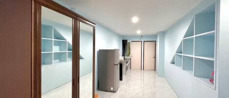 A hallway with a sliding door, a refrigerator, and a window with shelves.