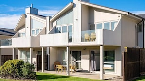 A modern two-story house with a balcony, large windows, and a well-maintained lawn.