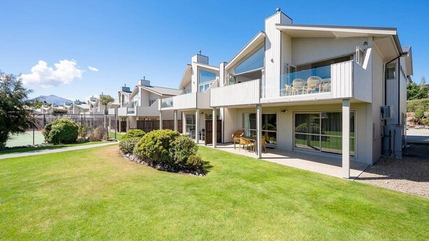 A modern multi-story residential building with large windows and a well-maintained lawn.