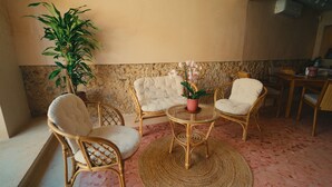 A cozy seating area with wicker chairs and a glass table, surrounded by a stone wall and a large potted plant. - La Garza, View of the interior garden. (Mérida)
