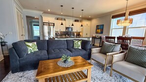 A living room with a sectional sofa, a wooden coffee table, and a dining area with chairs and a table. - Poipu 3BR/3BA corner villa, poolside, A/C (Koloa)