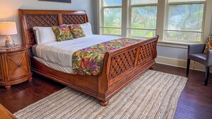 A bedroom with a wooden bed, a nightstand, a lamp, a painting, and large windows with a view of trees. - Poipu 3BR/3BA corner villa, poolside, A/C (Koloa)