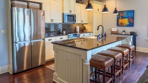 A modern kitchen with a stainless steel refrigerator, a microwave, and a large island with bar stools. - Poipu 3BR/3BA corner villa, poolside, A/C (Koloa)