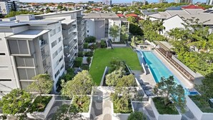 A modern apartment complex with a swimming pool, green spaces, and a view of the cityscape. - Balcony Views, Parking, Pool & Gym | Walk to CBD (Spring Hill)