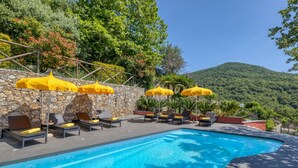 Une piscine entourée de murs de pierre et de verdure, avec des chaises longues et des parasols jaunes.