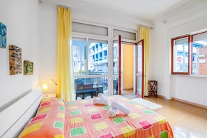 Habitación de hotel con cama, una mesita, una silla, un balcón con vistas a la ciudad y una ventana que da a la calle.