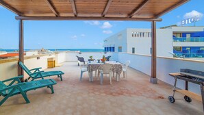A covered outdoor patio with hexagonal tiles, a table set for dining, and a grill. - Sunny Sea-View Terrace in Torre dell’Orso, Melendugno, Italy (Melendugno)