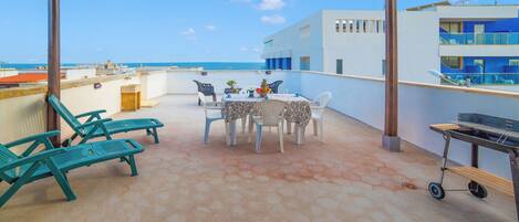 A covered outdoor patio with hexagonal tiles, a table set for dining, and a grill.