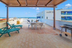 Eine überdachte Terrasse im Freien mit sechseckigen Fliesen, einem Esstisch und einem Grill.