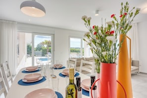 A dining area with a table set for four, a bottle of wine, and a vase with flowers. - Pool Villa Ora in Nature, Rakalj, Croatia (Rakalj)