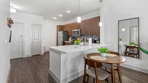 A modern kitchen with white cabinetry, a central island, and a dining area with a wooden table and chairs.