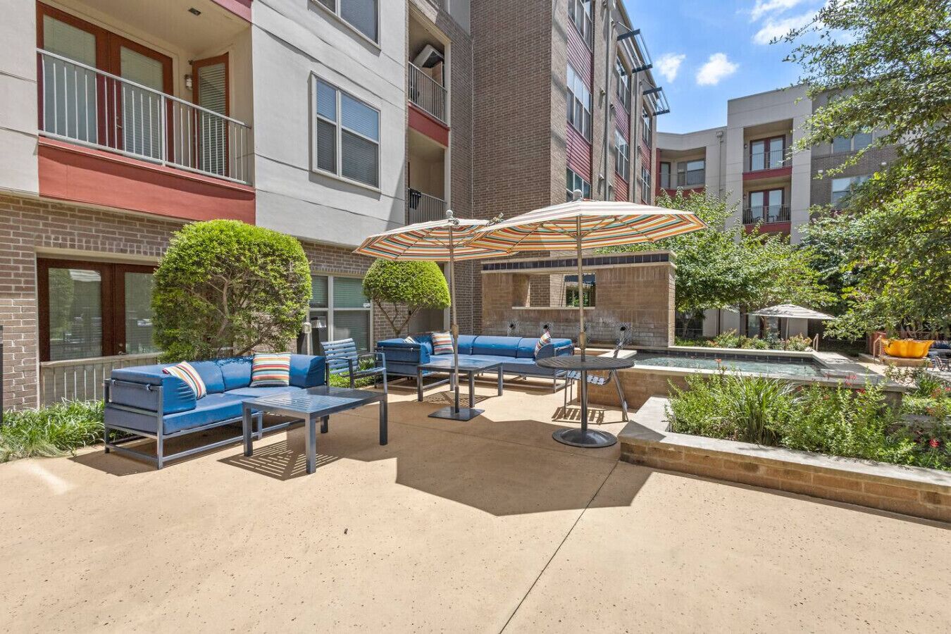 An outdoor patio area with blue seating, a small pool, and a brick building in the background.