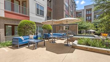 An outdoor patio area with blue seating, a small pool, and a brick building in the background.