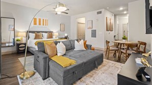 Una sala moderna con un sofá seccional gris, una lámpara de pie, un comedor con sillas de madera y una mesita pequeña.