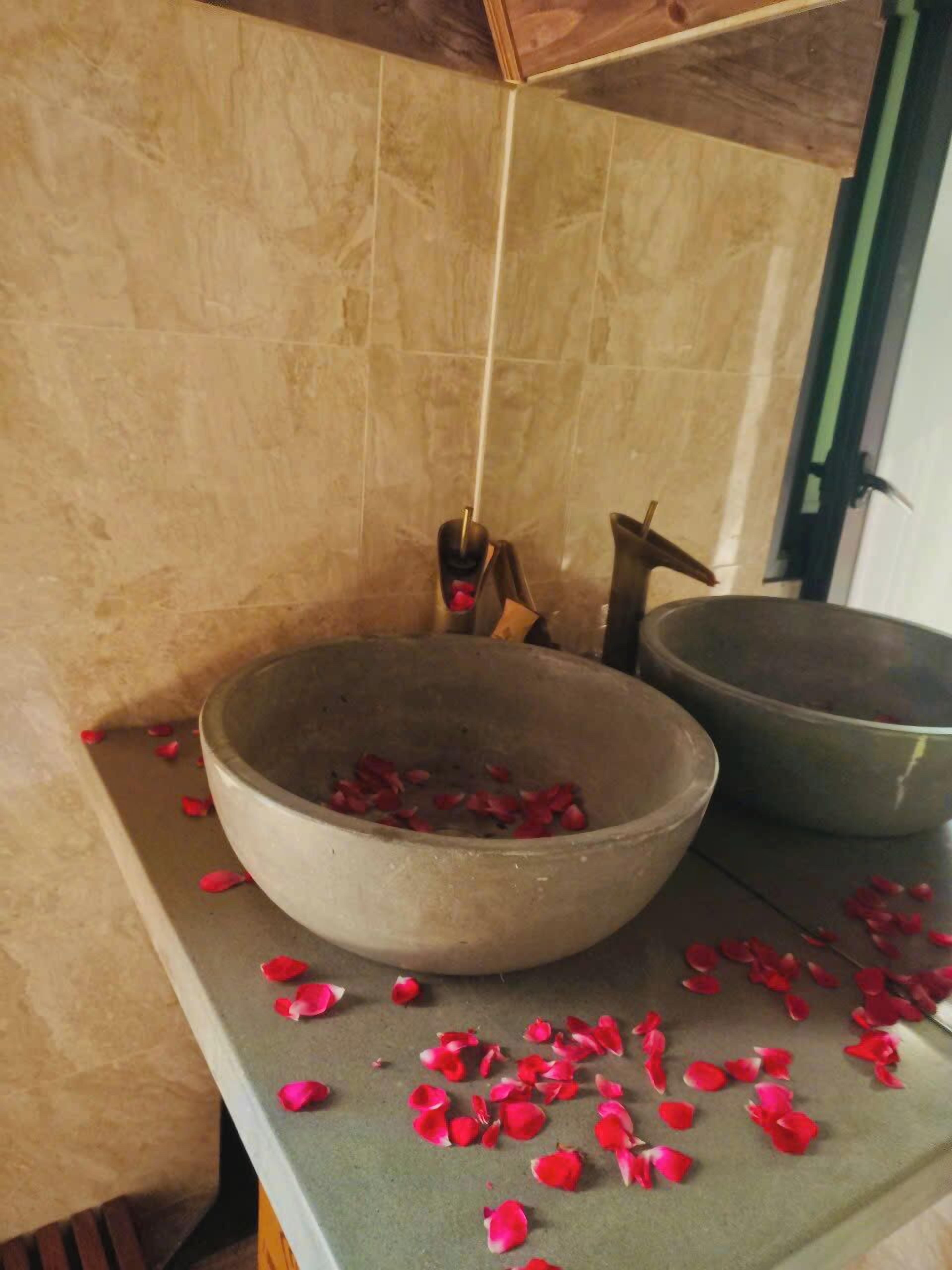 Une salle de bain avec une grande vasque en pierre remplie de pétales de rose, un seau en bois et un récipient en métal.