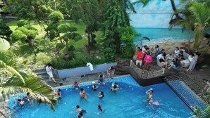 A swimming pool surrounded by lush greenery and a beach scene. - Luong Son Retreat (Luong Son)