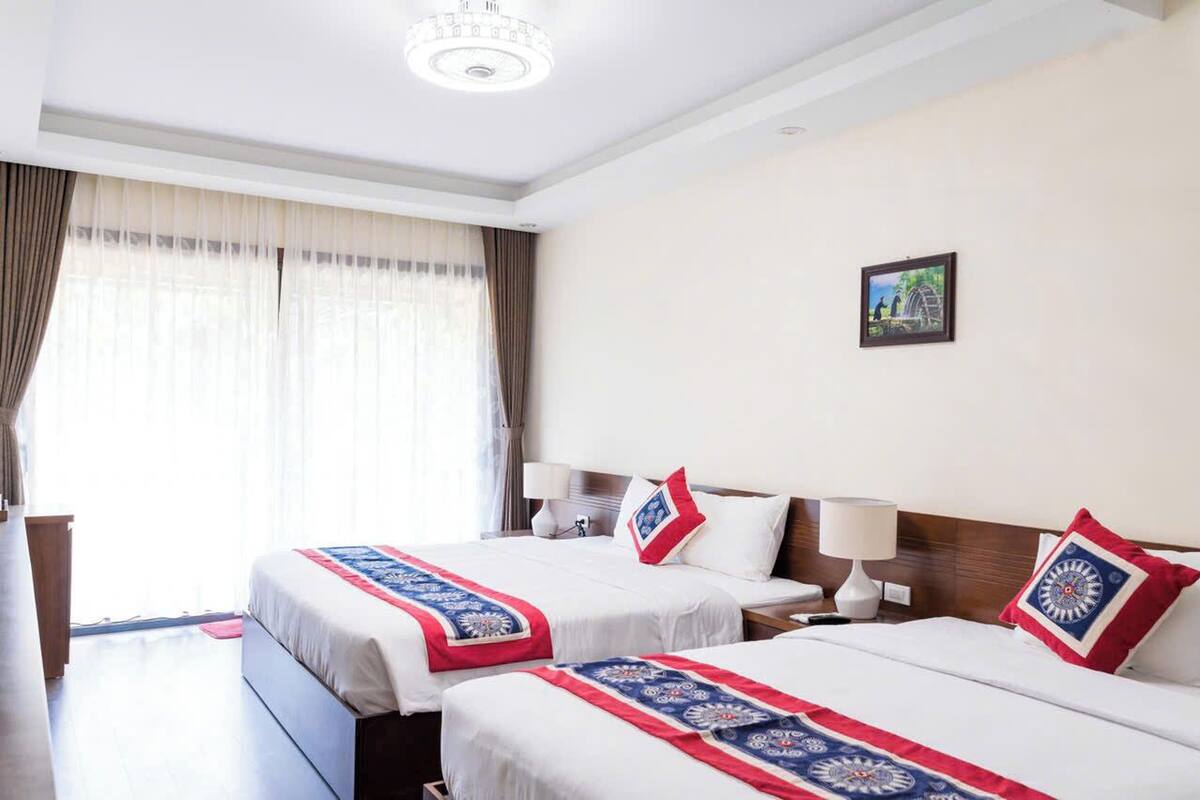 Habitación de hotel con dos camas, cada una con colcha de diseño rojo y azul, cabeceros de madera, lámparas de noche y un cuadro enmarcado en la pared.