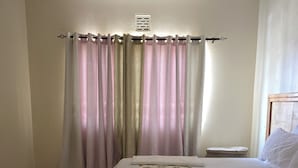 Un dormitorio con cama, mesita de noche y un ventano con cortinas, además de un respiradero en el techo.