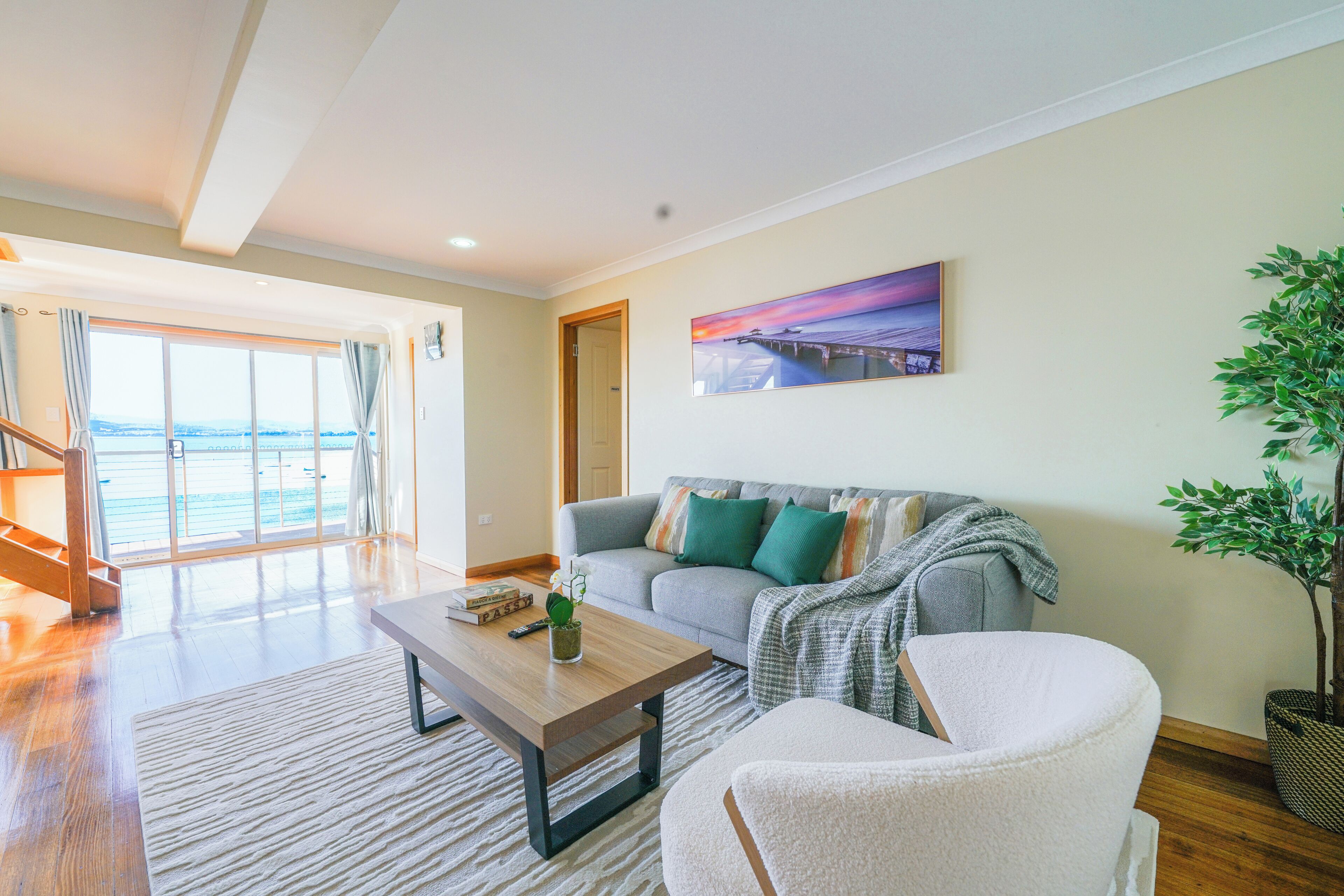 A spacious living room with a sofa, a coffee table, and a chair. There is a large window with a view of the outdoors.