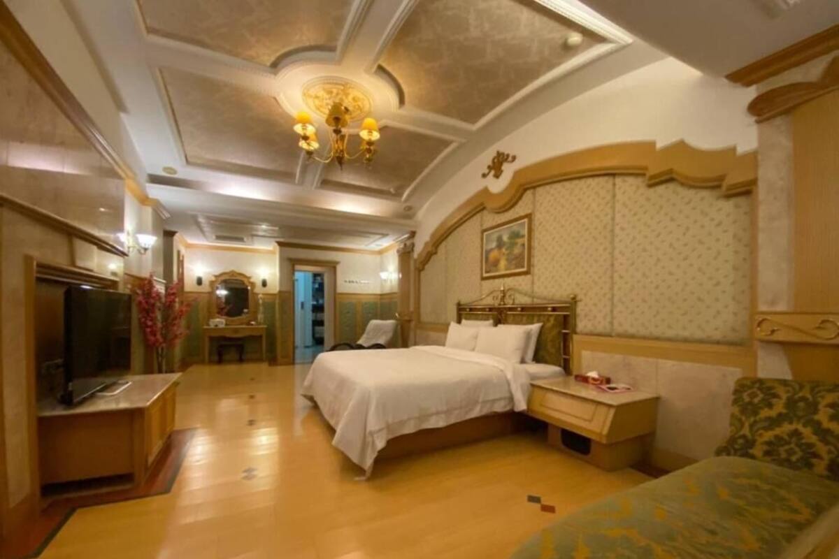 A hotel room with two beds, a desk, a television, and a chandelier.