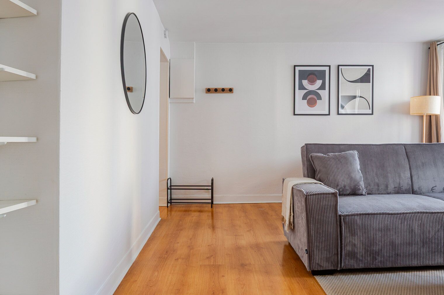 A modern living room with a grey sofa, a wooden floor, white walls, and a mirror.