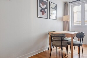 Uma sala de jantar com mesa de madeira e quatro cadeiras, uma luminária e duas pinturas abstratas na parede.