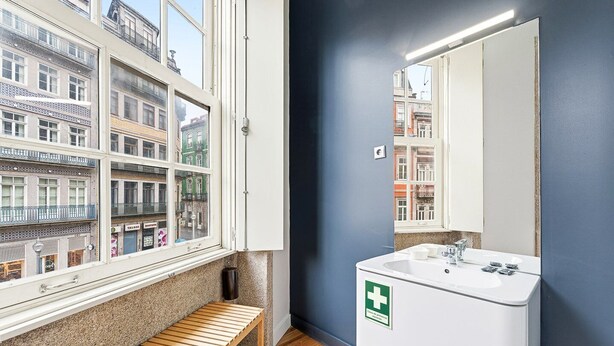Un bagno moderno con un'ampia finestra, un lavandino bianco con il simbolo della croce verde e una panca di legno.