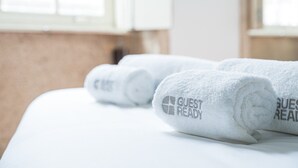 Camera d'albergo con asciugamani bianchi ordinatamente piegati su un letto, ognuno con ricamato il testo "GUEST READY".