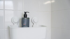Une salle de bain avec un lavabo blanc, une bouteille de shampoing noire et un porte-savon blanc.