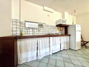 A kitchen with a tiled backsplash, a white refrigerator, and a wooden chair. - " Colori di Sardegna Belvedere " (Bari Sardo)