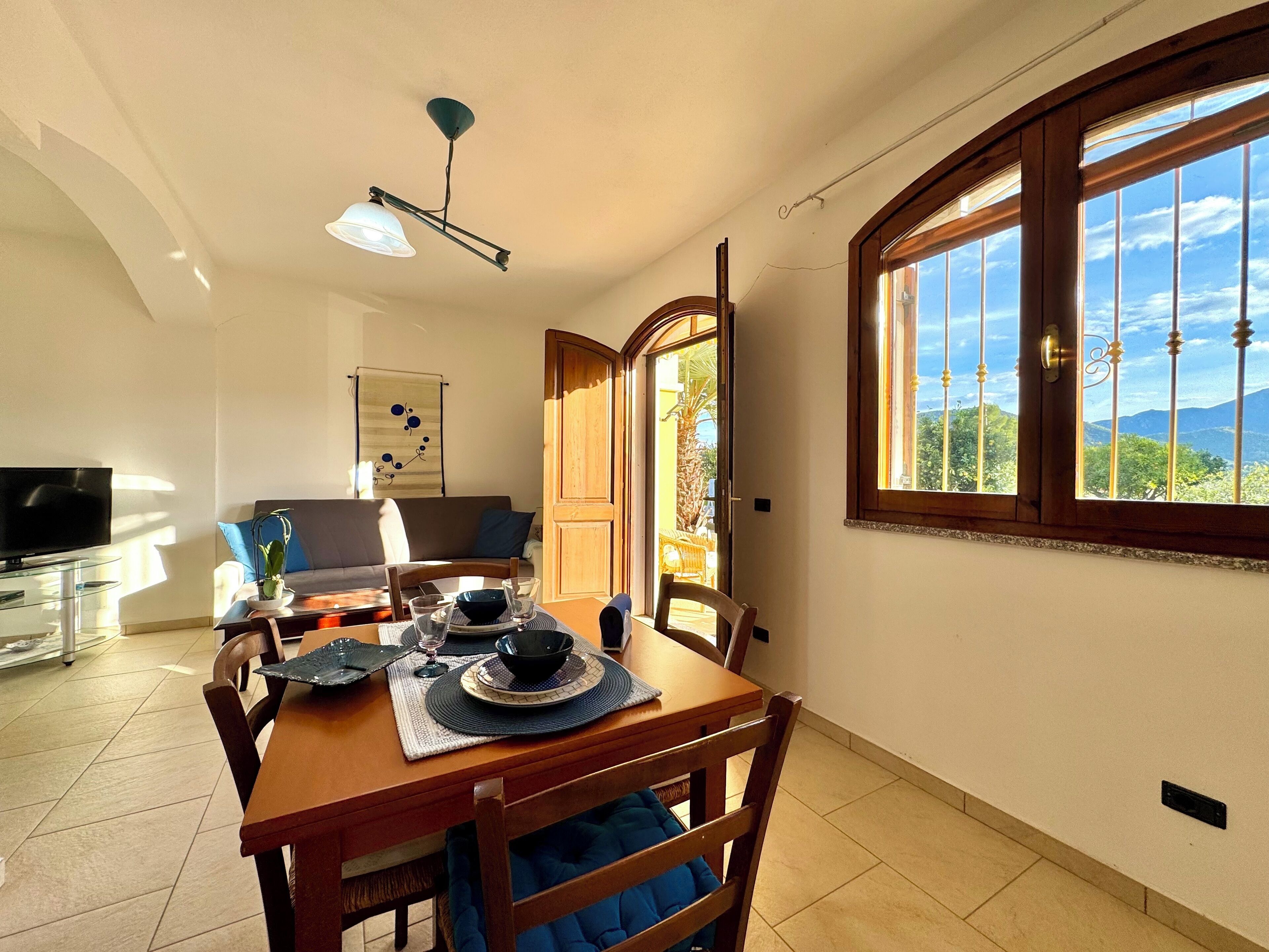 A dining area with a table set for two, a television on a stand, and a large window with a view of the outdoors.